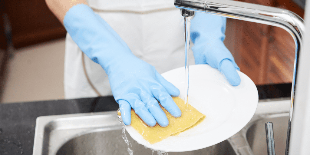 A photo of a woman's hands in rubber gloves washing a plate.