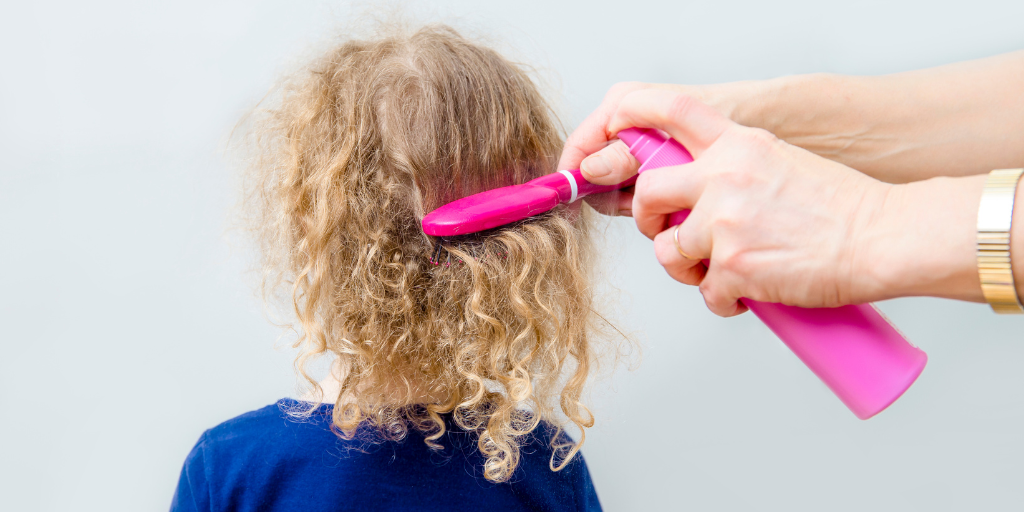 A photo of a parent combing child's hair. Avoid cyclopentasiloxane in skin care and hair care.