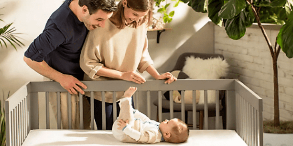 Naturepedic organic crib mattress. A photo of a baby lying on a firm baby mattress made by Naturepedic, and his parents playing with him.