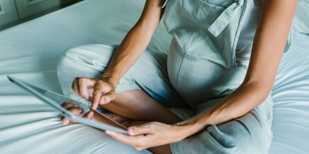 a photo of a woman sitting of a bed with a tablet.