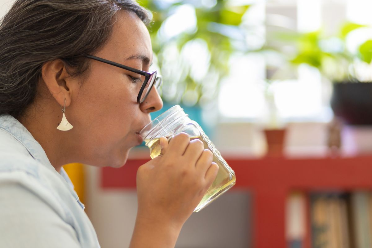 A photo of a woman drinking hot tea from a mason jar.